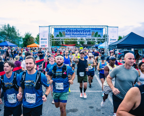 2025OHM_01 Runners start the Oktoberfest Half Marathon under a white starting banner with blue lettering